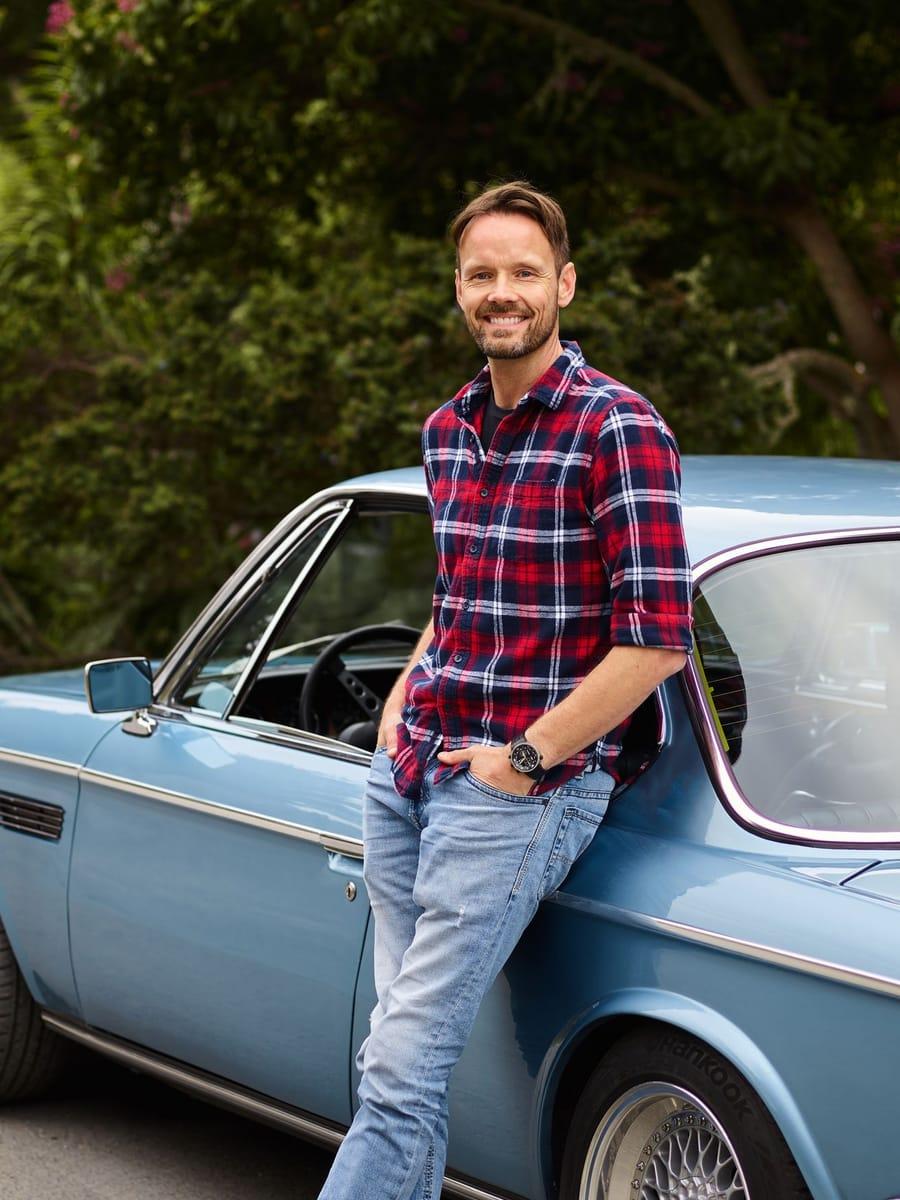 Automobilist leunt ontspannen tegen zijn auto